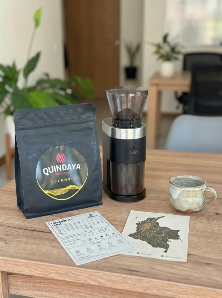 Café de especialidad sostenible para oficinas: bolsa de Quindaya Colombia, molinillo, taza y ficha de trazabilidad sobre una mesa.
